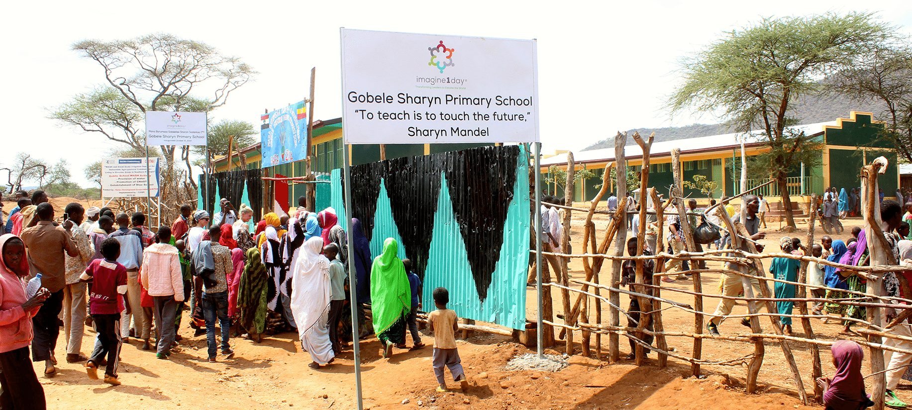 The front gate to the Gobele Sharyn Mandel Primary School, with a sign that quotes "To teach is to touch the future".